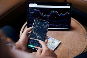 Close-up of a person trading stocks using a smartphone and a tablet