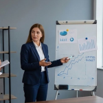 A woman in a navy suit presents a line graph to three colleagues taking notes