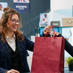Shop assistant handing a burgundy bag to a customer in a stylish London boutique with posters and plants in background