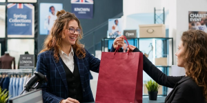 Shop assistant handing a burgundy bag to a customer in a stylish London boutique with posters and plants in background