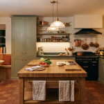 Cosy kitchen with wooden island, vegetables, copper pans, and a breakfast nook with plants and natural lighting